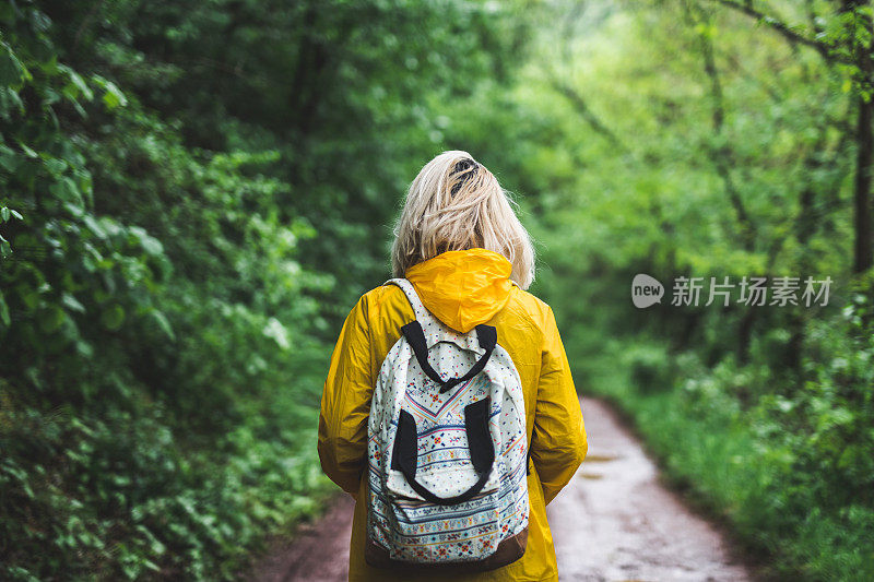 后视图的女人在黄色雨衣走在道路上的森林