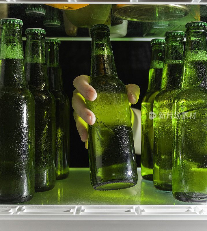那只手伸向啤酒瓶。冰箱的架子上有绿色的啤酒瓶和凝结的水珠。