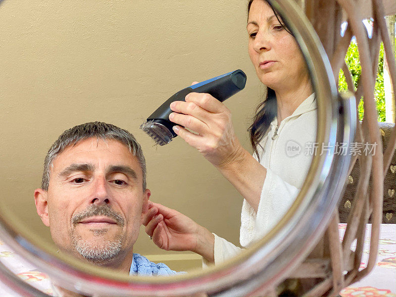 新冠肺炎疫情期间，妻子为丈夫剪头发。男人的脸映出在镜子里。呆在家里。生活在lockdow