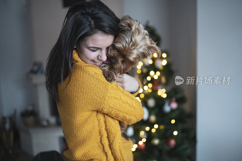 一个年轻的女人和她的小狗依偎在圣诞树旁