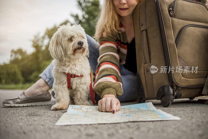 一个小女孩坐在一个手提箱旁边，抚摸着她的狗