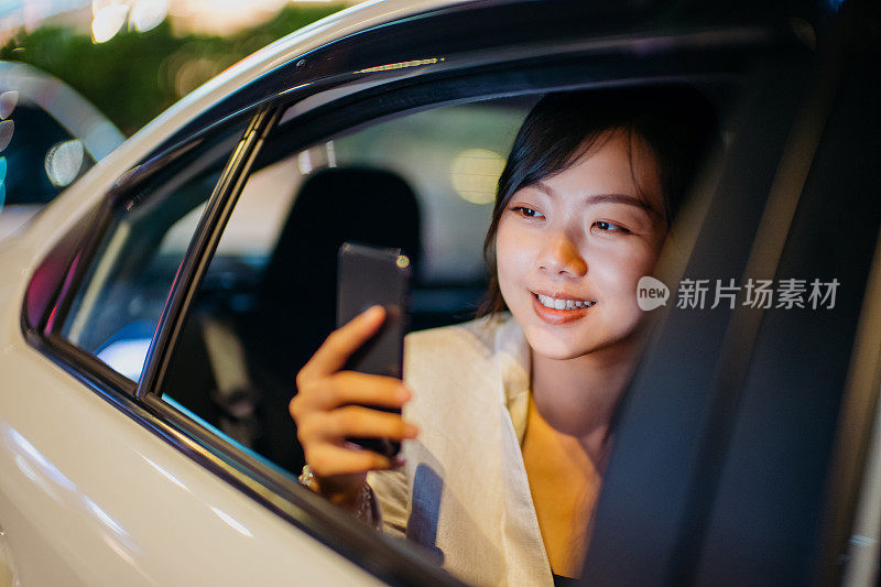 年轻的亚洲女商人使用智能手机，在一个夜晚的城市乘用车座位上拍照