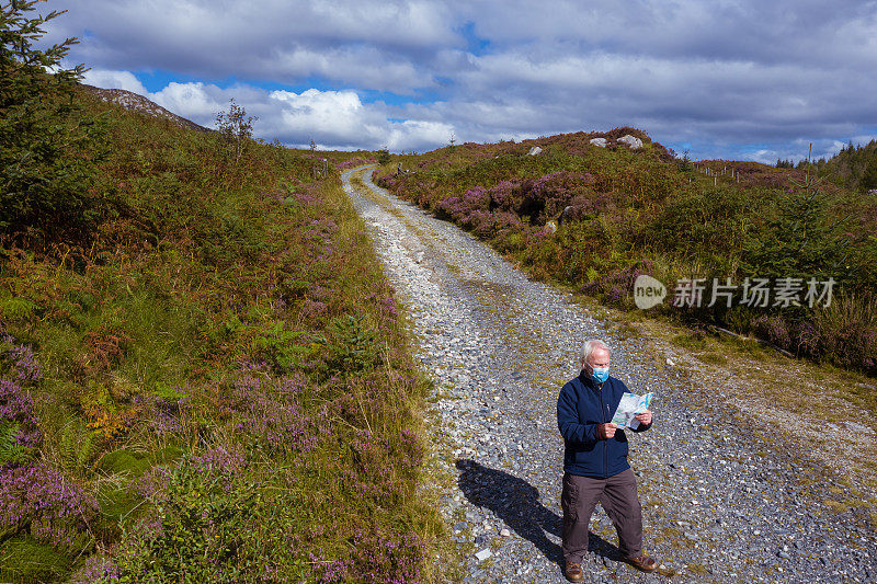 在苏格兰西南部邓弗里斯和加洛韦偏远地区的一条土路上，一名戴着口罩的老人站在看地图的无人机拍摄的画面