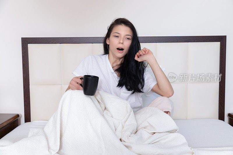 年轻女性醒来后一边喝咖啡一边打哈欠