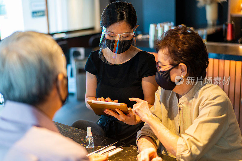 服务员戴着面罩和面罩，为资深亚洲夫妇点菜。