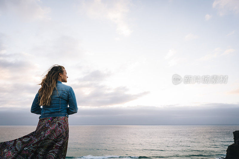 年轻女子在多风的海岸悬崖上休息