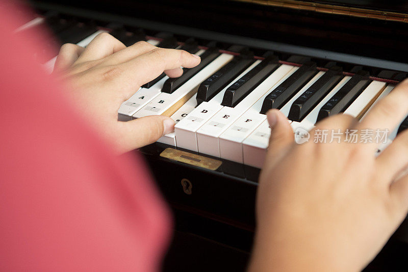特写少年的手在钢琴上与写在键上的音符，看在肩上