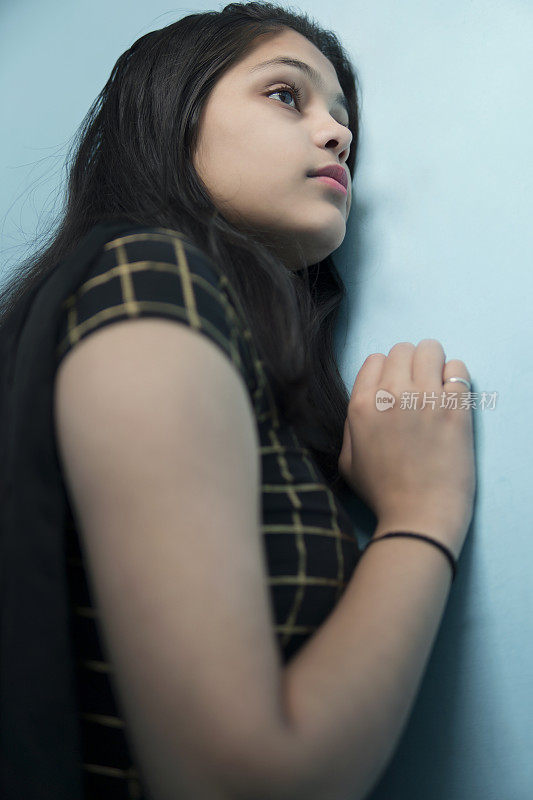 一个悲伤而安详的印度女人站在墙边沉思着。
