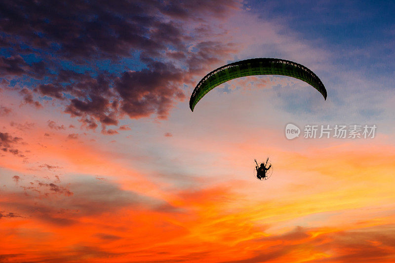 跳伞日落景观降落伞飞行在软焦点。夕阳下的Para-motor飞行剪影。剪影的滑翔伞飞行在傍晚的天空与日落。