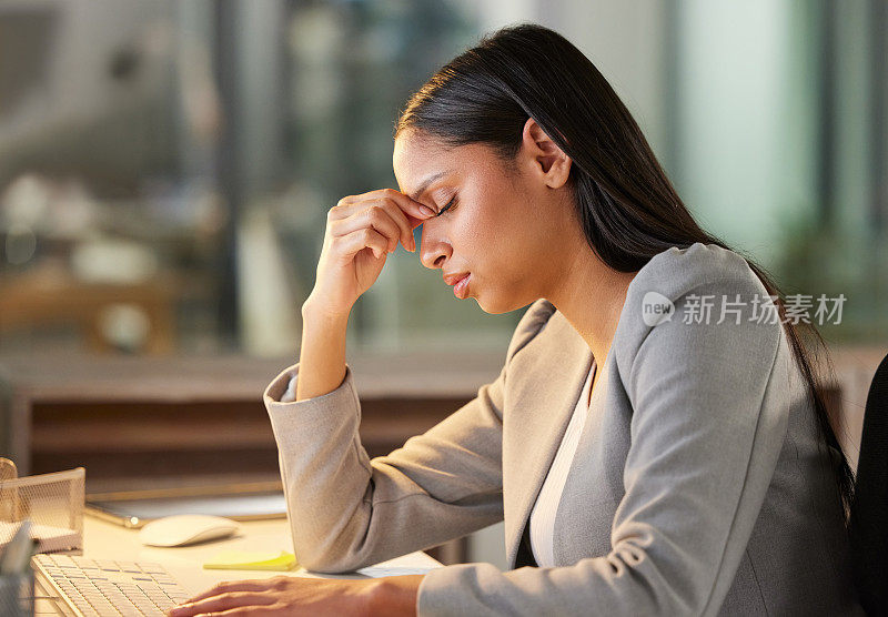 在现代办公室里，一位年轻的女商人坐在办公桌前使用电脑，看上去压力很大