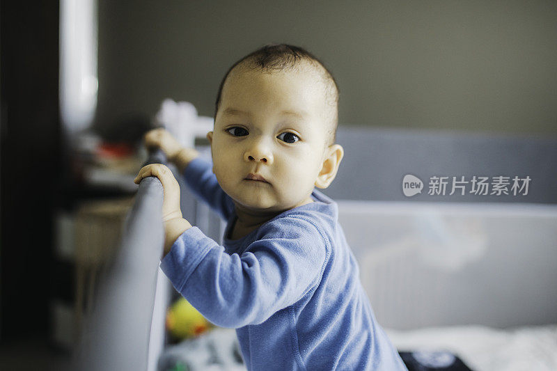 人像亚洲宝宝站着，抱着床架