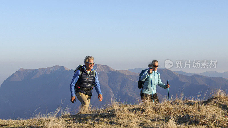 成年夫妇沿着长满青草的山脊徒步旅行