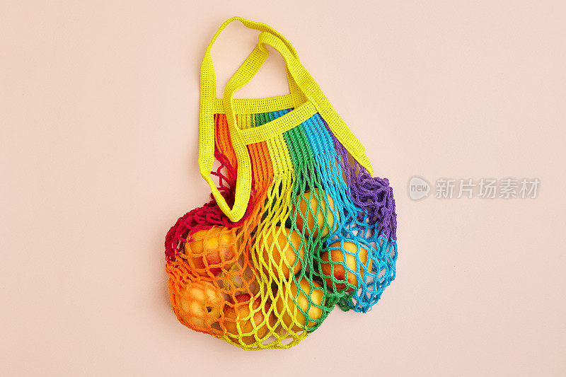 静物彩虹色网状购物袋与有机生态蔬菜和水果在绿色背景。爱护环境，摒弃塑料概念