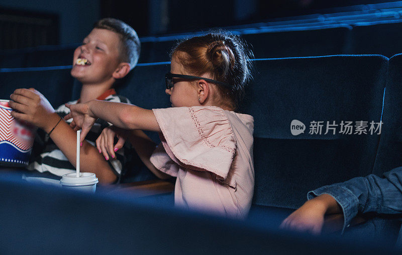 小孩子戴着3d眼镜，吃着爆米花，在电影院看电影。