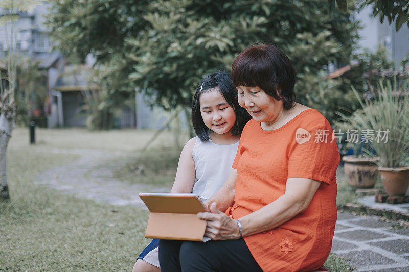 亚裔华人活跃的老年妇女和孙女周末在后院用笔记本电脑学习