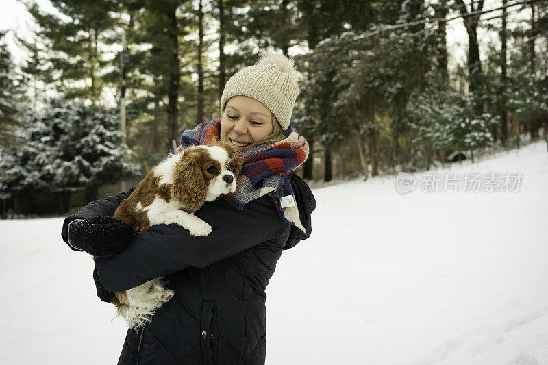 在雪地里，一名女子抱着她的查理骑士猎犬