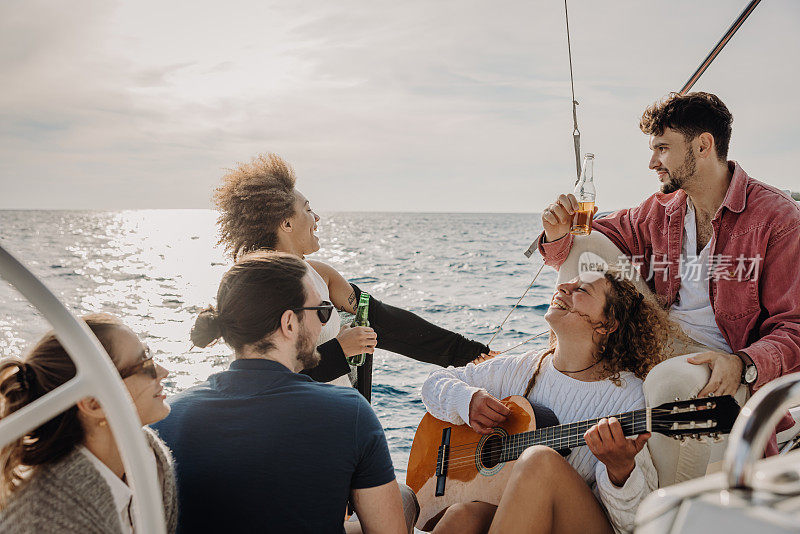 晚上，当她的朋友们在帆船的甲板上共享啤酒时，拿着吉他的女人微笑着