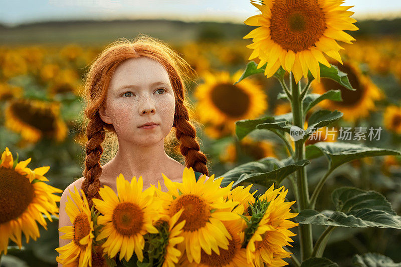 一个红头发，长着雀斑的美丽女孩站在向日葵丛中