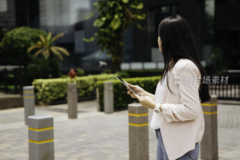 亚洲成年人在街上拿着平板电脑抬头看