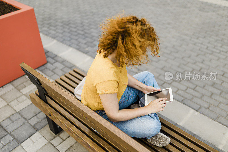 一个女人坐在长凳上看着平板电脑的照片