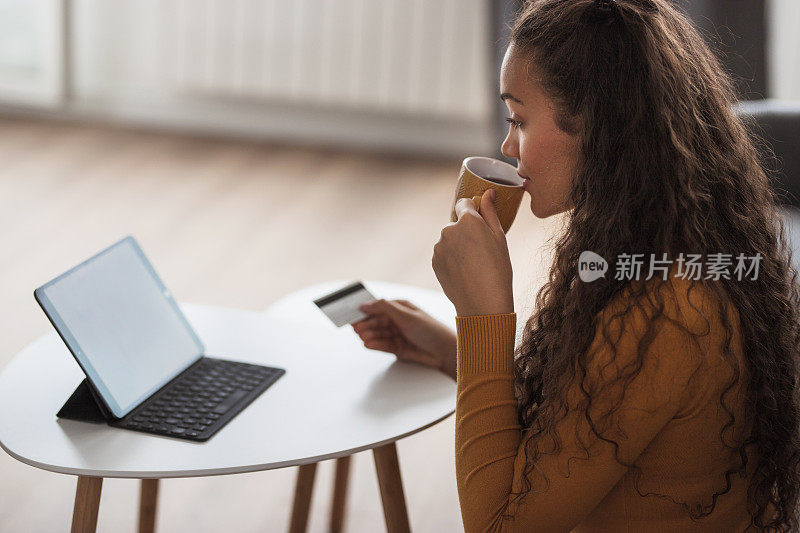 快乐的年轻女子在网上购物时喝着咖啡