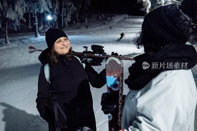 两个女人晚上在灯火通明的滑雪坡上聊天。