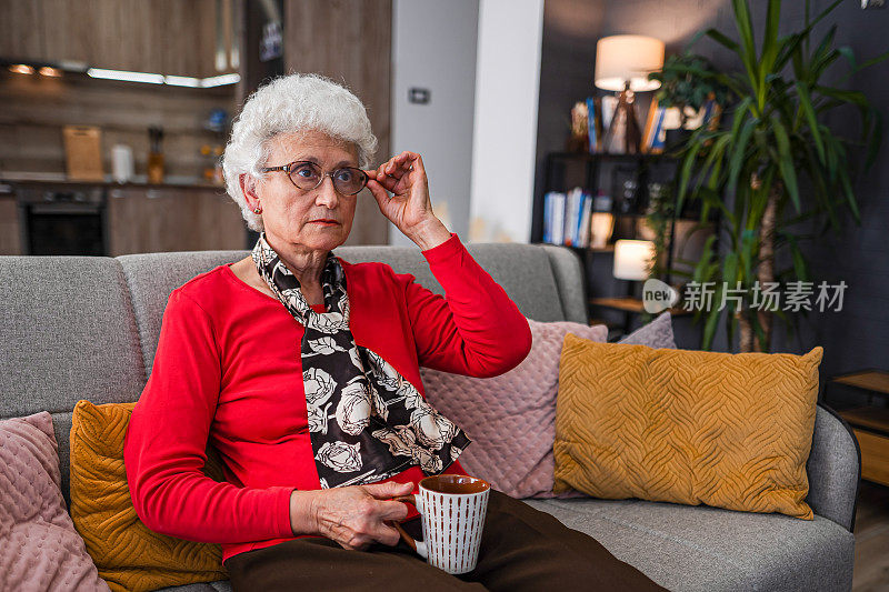 退休的老女人在客厅喝热茶和看电视