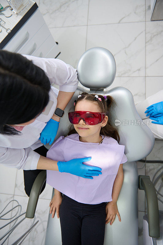 女牙科保健师在儿童牙科诊所预约期间与一个小病人交谈