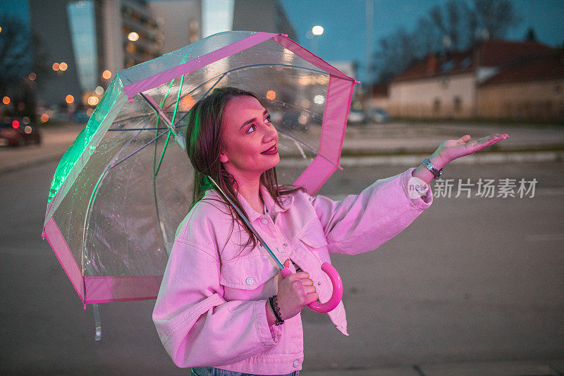 一个微笑的女人在城市里走来走去，伸出她的手看看是否还在下雨