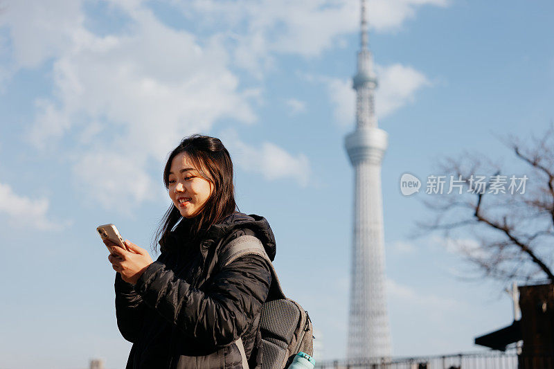 冬季，亚洲女游客在东京天空树前使用智能手机