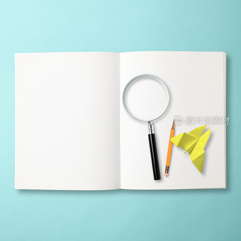 折纸黄蝴蝶，放大镜和黄色铅笔在打开空白笔记本