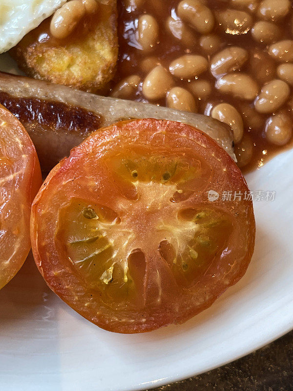 全英式油炸早餐食材，单面煎蛋，香肠，烤西红柿和两个土豆饼放在一个白色盘子里，高架视图