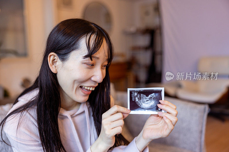 快乐的孕妇正在展示未出生婴儿的超声波照片