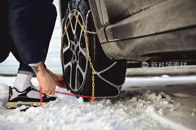 在冬天的路上，一名男子正在给一辆汽车装雪地轮胎链条。