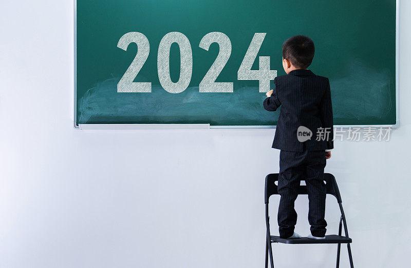 年轻的亚洲男孩在黑板上写新年数字2024