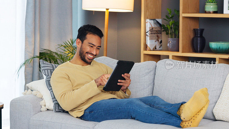 快乐，放松，亚洲男人用平板电脑和沙发在家里玩社交媒体，聊天或流媒体。数码、应用和日本男性在客厅微笑gif、表情包或网络、帖子和在线交流