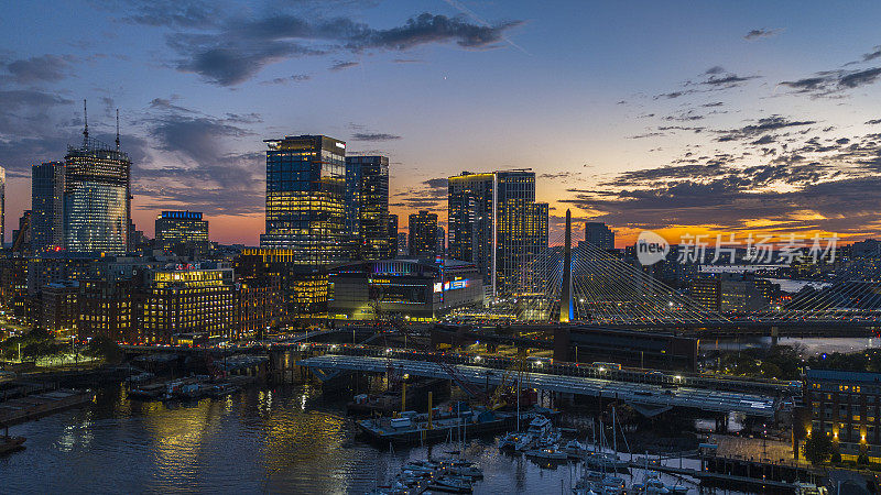 日落时的现代城市天际线和著名的伦纳德·p·扎基姆邦克山纪念桥。波士顿港前面有驳船和游艇。