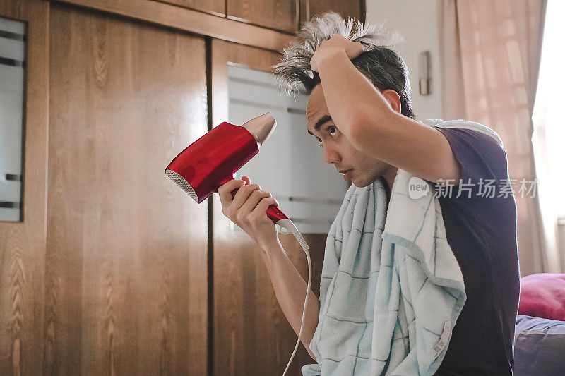 亚洲男人在卧室里用吹风机吹头发