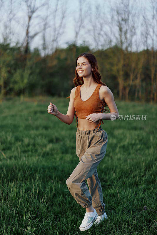 一个身材健美的女人在公园的绿草地上跑着，头发飘散着，在夕阳的余晖中锻炼着