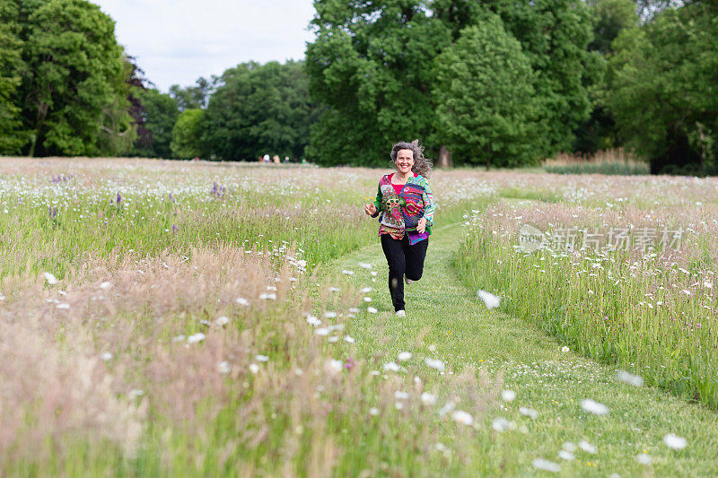 一位年长的妇女在一条小径上跑步，这条小径穿过长满野花的草地