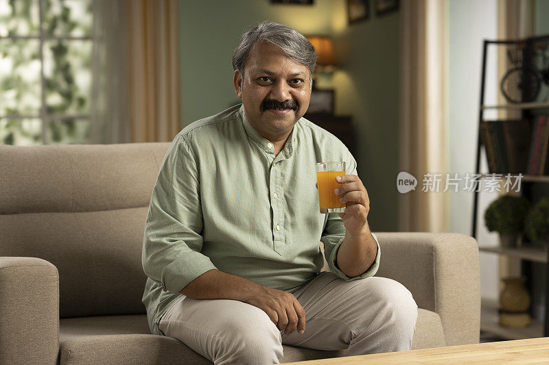 快乐的老人坐在家里的沙发上喝着橙汁。股票辐透