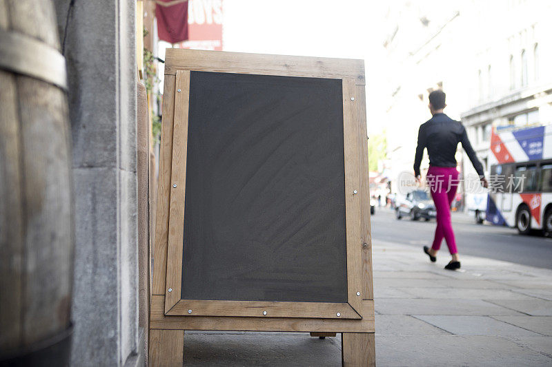 一名男子在伦敦市中心的人行道上走过一块黑板