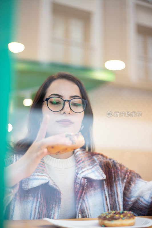 年轻的黑发女人正在吃甜甜圈。