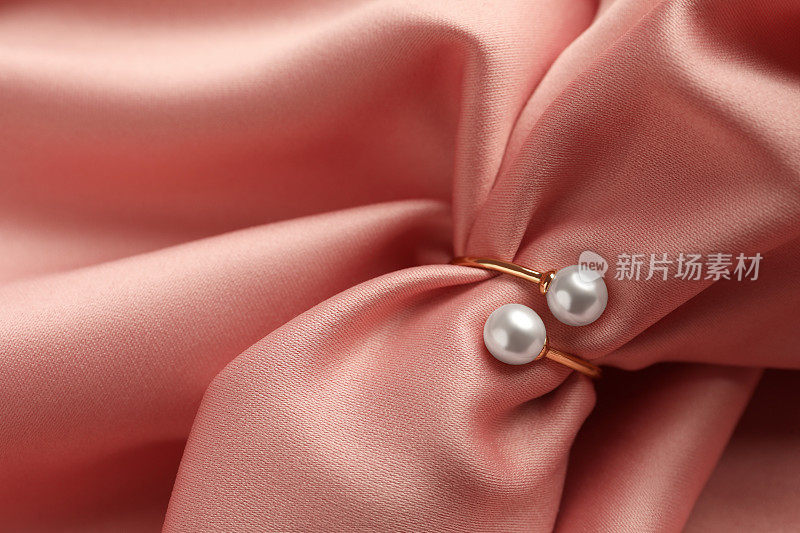 优雅的金戒指与珍珠粉红丝绸，特写