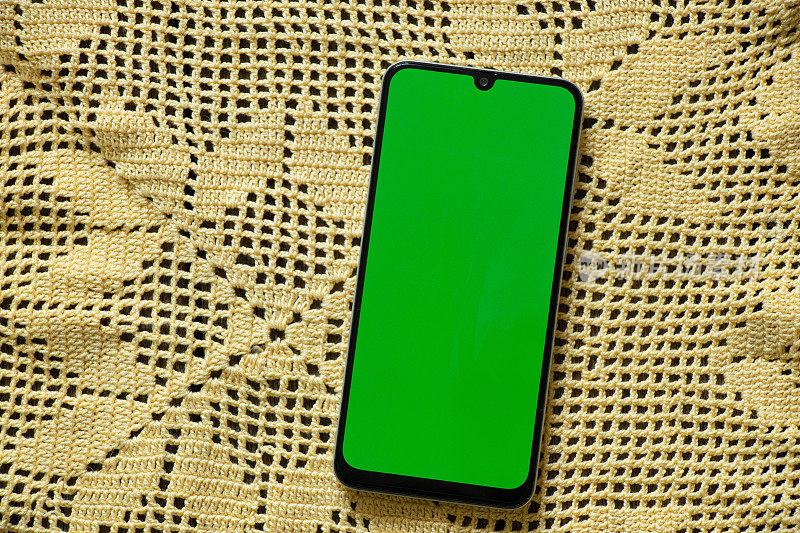 绿色屏幕的手机放在一张黄色蕾丝餐巾上