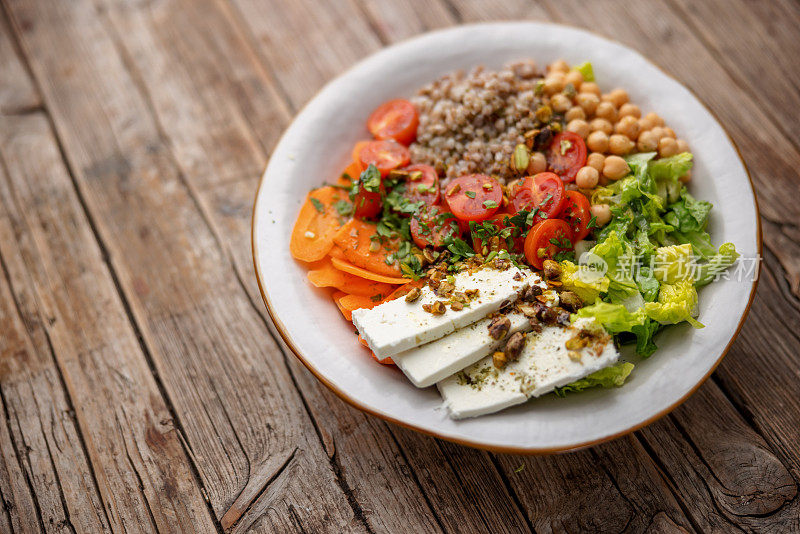 彩色的健康沙拉装在白色的陶瓷盘子里，放在木制的桌子上