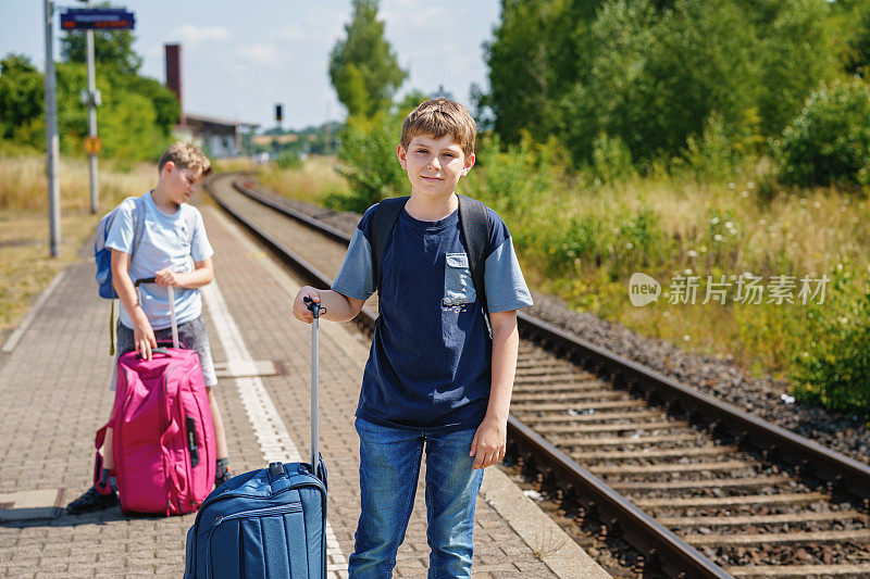两个孩子，男生提着行李箱准备去夏令营。快乐的孩子，兄弟姐妹，双胞胎兄弟去旅行，家庭公路旅行等火车。