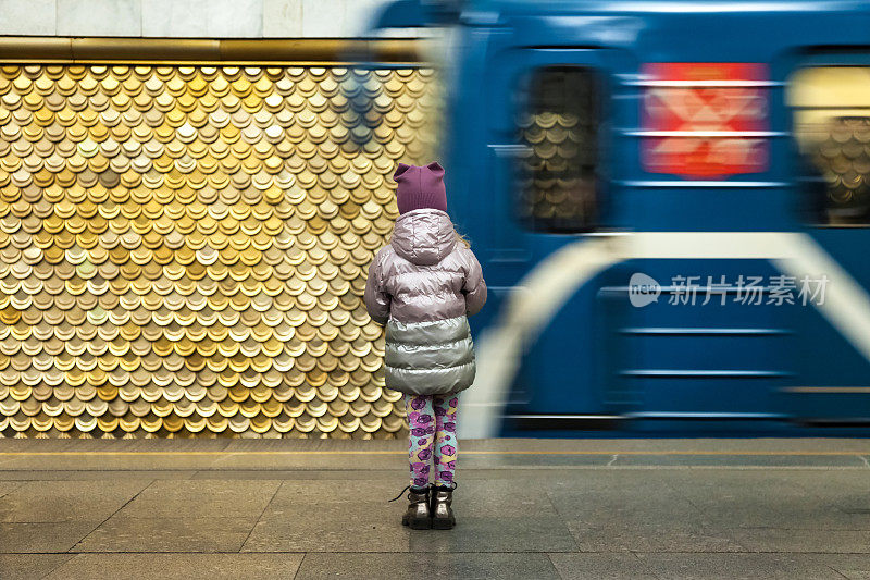 后视图5岁的小女孩站在地铁月台前的移动列车。小乘客在地铁里的背影。公共城市交通概念。复制文本空间