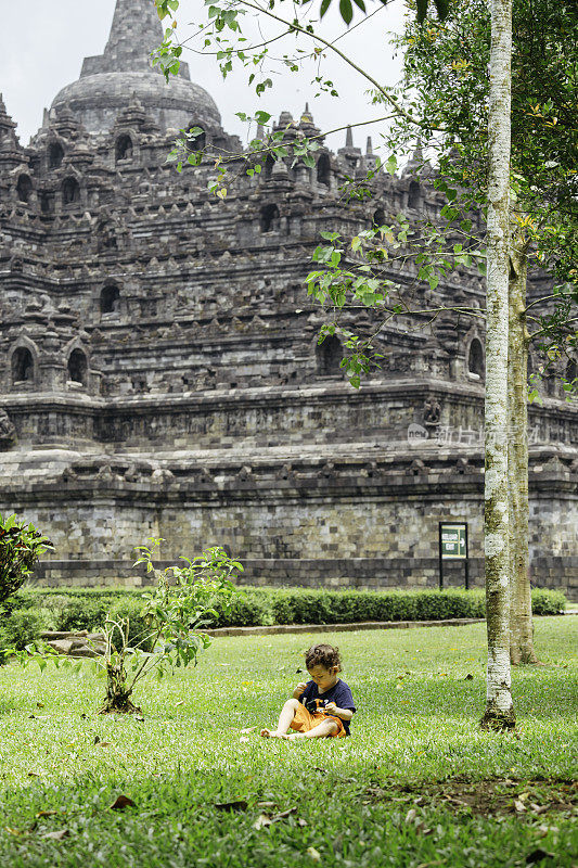 一个小孩走在草地上，背景是婆罗浮屠寺