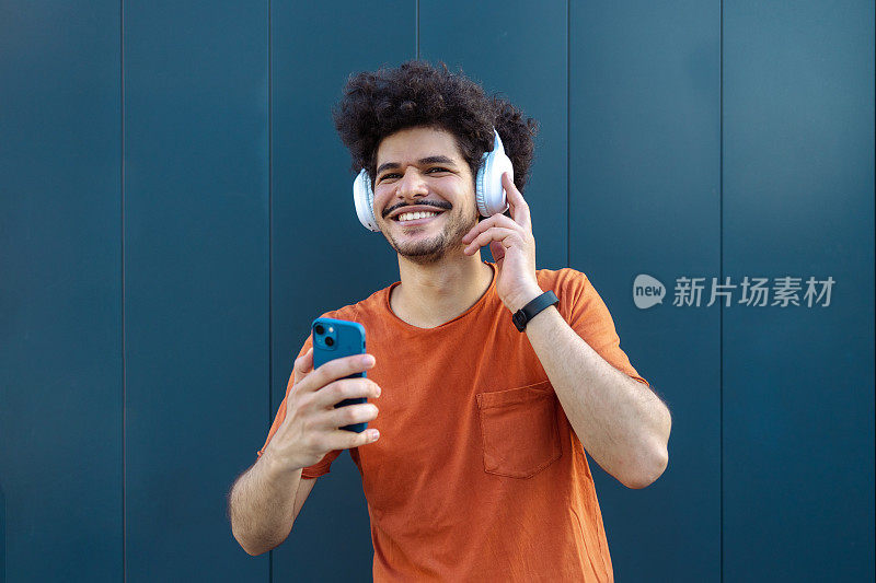 一个中东男人在蓝色的墙前用智能手机听音乐